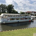 MS Stadt Verden - Flotte Mittelweser Ein weißes Passagierschiff auf einem ruhigen Fluss neben einem kleinen Hafen mit Gebäuden im Hintergrund.