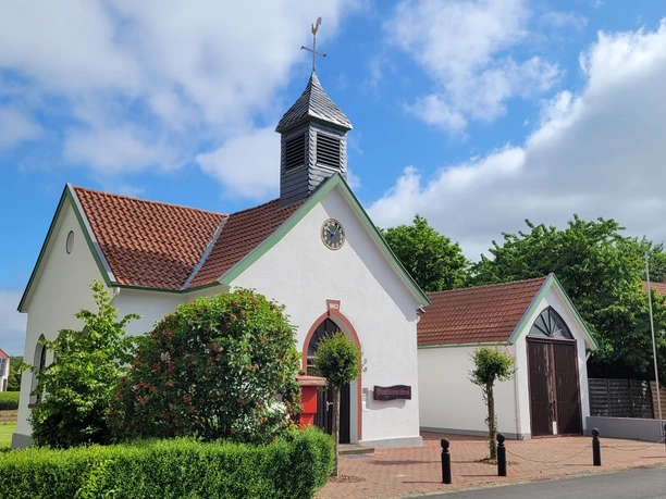 Feuerwehrmuseum Schröttinghausen Weißes Gebäude mit Satteldach, rotem Tor und kleinem Kirchturm mit Wetterfahne, neben Grünflächen.