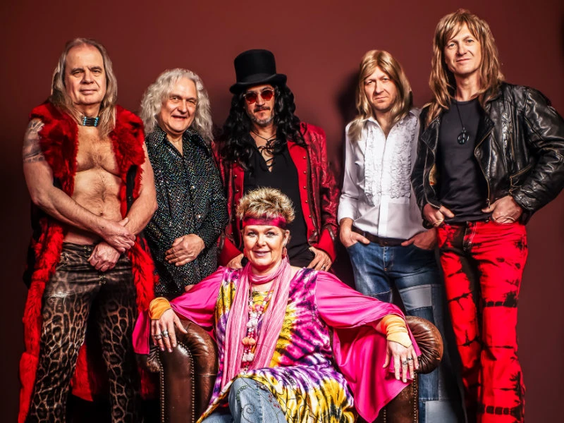 major_healey_web.jpg Sechs Bandmitglieder in bunter, retro-inspirierter Kleidung posieren vor einem roten Hintergrund.