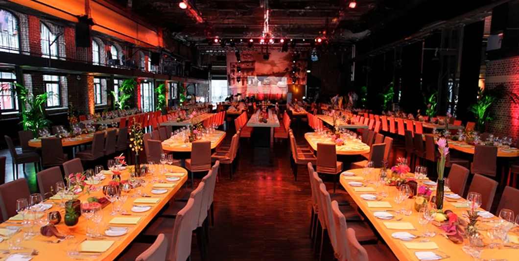 mSa Firmenevents Veranstaltungshalle im Industrielook mit gedeckten Banketttischen in atmosphärischer BeleuchtungEvent hall in an industrial style with covered banquet tables and atmospheric lighting