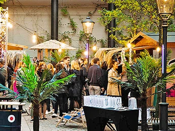 mSa Club Tropicana Club Tropicana Sommerfest: Menschen stehen im Setting mit Bast-Sonnenschirmen und PalmenClub Tropicana summer party: people in a setting with bast sunshades and palm trees