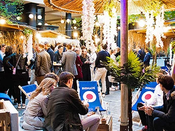 mSa Club Tropicana Club Tropicana Sommerfest: Vorne sitzen Personen im Kreis auf Liegestühlen und im Hintergrund steht eine MenschenmengeClub Tropicana Summer Festival: people are sitting in a circle on sun loungers at the front, with a crowd in the background.