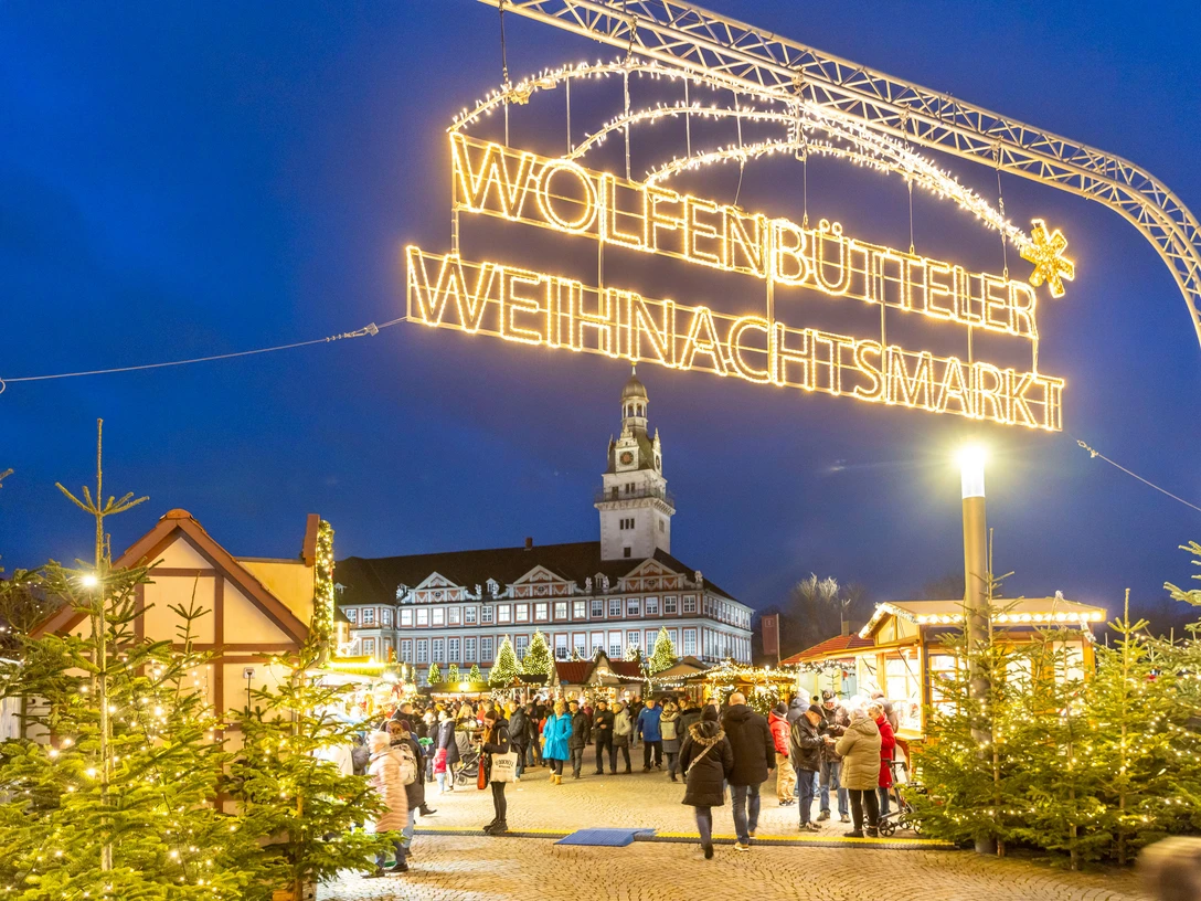 Weihnachtsmarkt Wolfenbüttel Leuchtender Schriftzug Wolfenbütteler Weihnachtsmarkt überspannt den Eingangsbereich zu einem stimmungsvollen MarktIlluminated Wolfenbüttel Christmas Market lettering spans the entrance area to an atmospheric marketOplyste Wolfenbüttel-julemarkedsbogstaver spænder over indgangsområdet til et stemningsfuldt markedVerlichte Wolfenbüttel Kerstmarkt belettering overspant de ingang van een sfeervolle markt