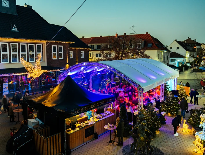Gänseliesels Weihnachtslounge Weihnachtslounge mit glitzernden Lichtern, überdachten Marktständen und einem Weihnachtsengel in Monheim.