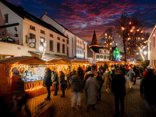 Der Monheimer Weihnachtsmarkt in der Altstadt Weihnachtsmarkt in Monheims Altstadt mit beleuchteten Ständen, Menschenmengen und dekorierten Bäumen.