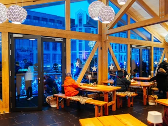 Das Winter-Chalet auf dem Monheimer Sternenzauber mit Eislaufbahn Winterliches Chalet mit Holzbänken und großen Fenstern, leuchtet in warmem Licht, Menschen sind zu sehen.