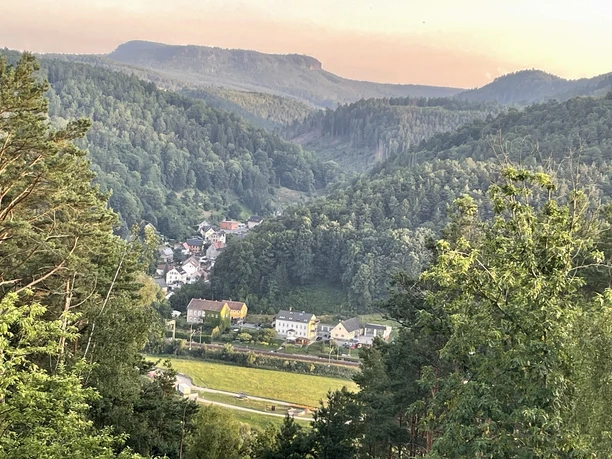 Uitzicht vanaf de Skywalk Zicht op een dorp in een beboste vallei, omringd door groene heuvels en bomen, in zacht avondlicht.