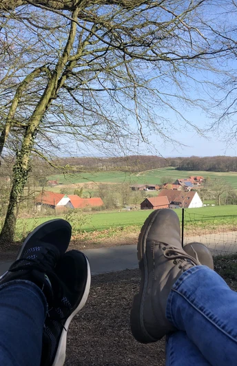 Blick aus der Waldschaukel Zwei Personen entspannen mit Blick auf eine idyllische, von Bäumen umrahmte, grüne Landschaft.