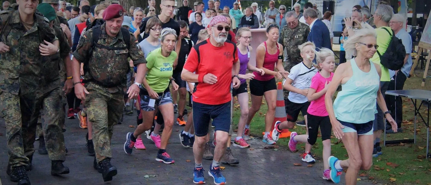 Volkslauf-Tag-der-Reservisten-Bad-Zwischenahn1.jpg Eine Gruppe von Läufern startet beim Volkslauf-Event in Bad Zwischenahn, angeführt von Reservisten in Uniform.