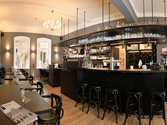 KÜPERs Bistro und Kaffeerösterei Ein großzügiger, stilvoll eingerichteter Bistro-Raum mit dunklem Mobiliar und Kronleuchter.