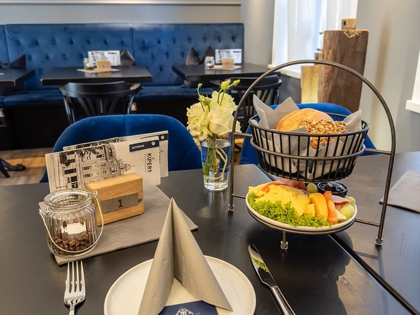 KÜPERs Frühstück Eleganter Frühstückstisch mit Brötchenkorb, Obstplatte, Gedeck und stilvoller Dekoration.