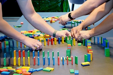 Drei Personen bauen ein Dominospiel auf mSa Team-Bash