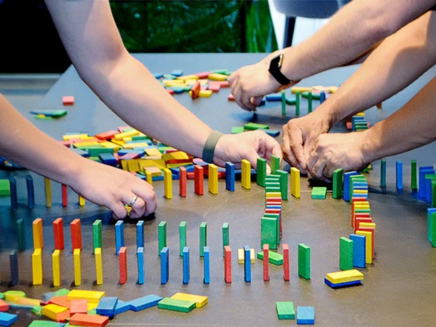 Three people are setting up a game of dominoes. mSa Team-Bash