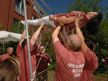 Teamparcours Teamparcours: Ein Team hebt eine Frau durch ein HindernisTeam obstacle course: a team lifts a woman over an obstacle