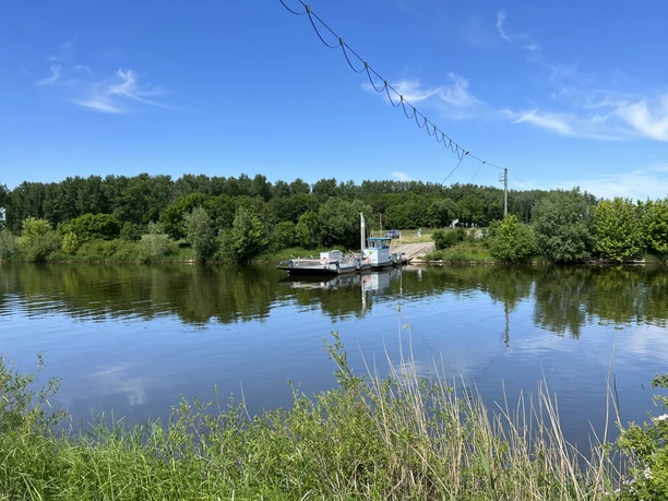 Schweringen Ferry The Schweringen ferry peacefully crosses a river, surrounded by green countryside and a clear sky.