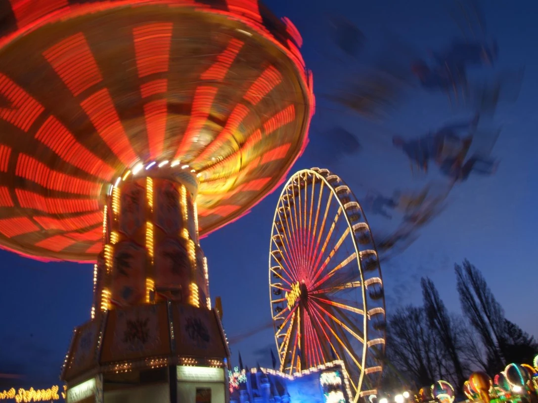 Ein beleuchtetes Karussell dreht sich vor einem erleuchteten Riesenrad im Abendhimmel.