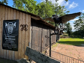Skulptur Adler Metallskulptur eines Adlers, breitet seine Flügel aus, vor einer rustikalen Holzscheune platziert.