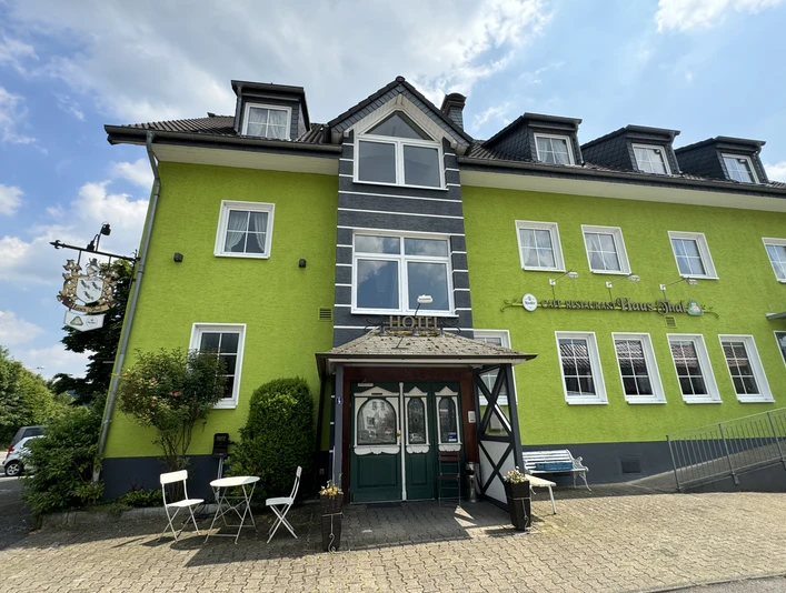 Haus Thal - Außenansicht Hotel in leuchtend grünem Gebäude mit Fachwerkdetails, Tischen und Stühlen im Freien, unter blauem Himmel.