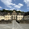 Schloss Ehreshoven Barockes Schloss mit hellgelben Fassaden, symmetrischen Flügeln und zentralem Torbogen, umgeben von Bäumen.