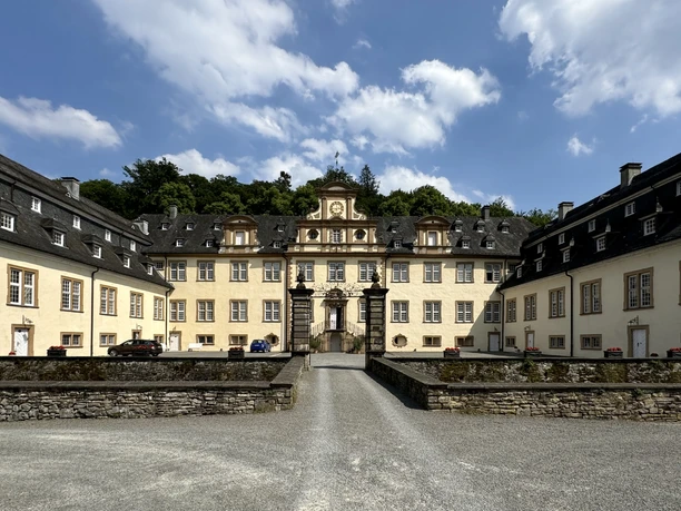 Schloss Ehreshoven Barockes Schloss mit hellgelben Fassaden, symmetrischen Flügeln und zentralem Torbogen, umgeben von Bäumen.