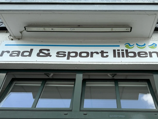 Logo - rad & sport liiben Fassade von "rad & sport lieben" mit einem Firmenlogo über großen Glastüren.