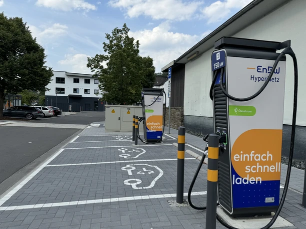 Ladesäule Drei EnBW-Ladestationen für Elektrofahrzeuge auf gepflastertem Parkplatz mit markierten Stellplätzen.