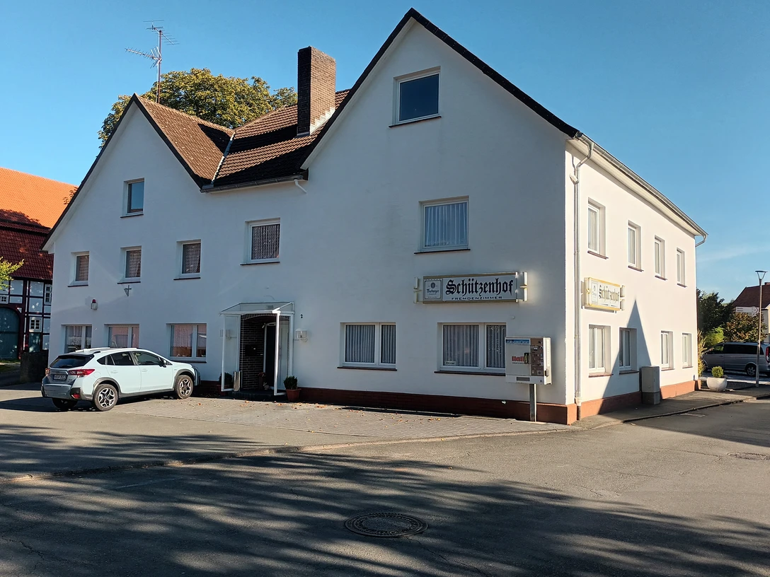 20221005_160541.jpg Großes, weißes Gasthaus an einer Straßenecke mit geparkten Autos und blauem Himmel im Hintergrund.