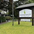 Gronauer Tannenhof Hotelschild des Tannenhofs auf grüner Wiese, umgeben von Bäumen und einem modernen Gebäude.