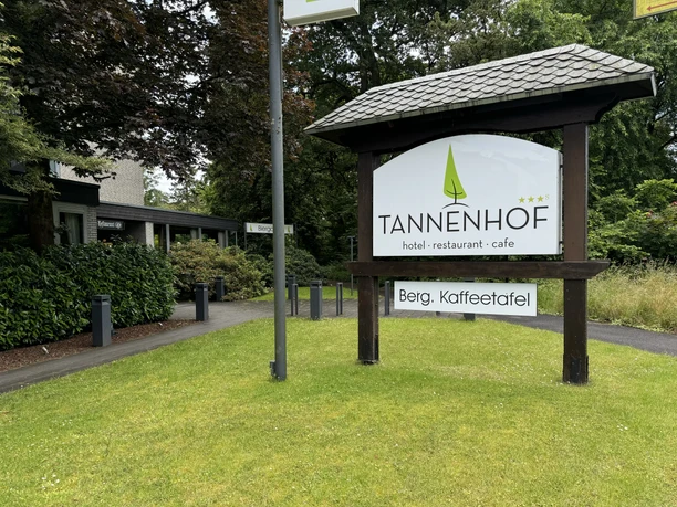 Gronauer Tannenhof Hotelschild des Tannenhofs auf grüner Wiese, umgeben von Bäumen und einem modernen Gebäude.