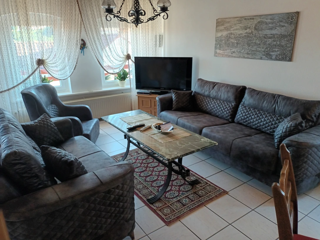 20230908_171435.jpg Ein helles Wohnzimmer mit zwei großen Sofas, einem Sessel, einem Teppich und einem Fernseher.