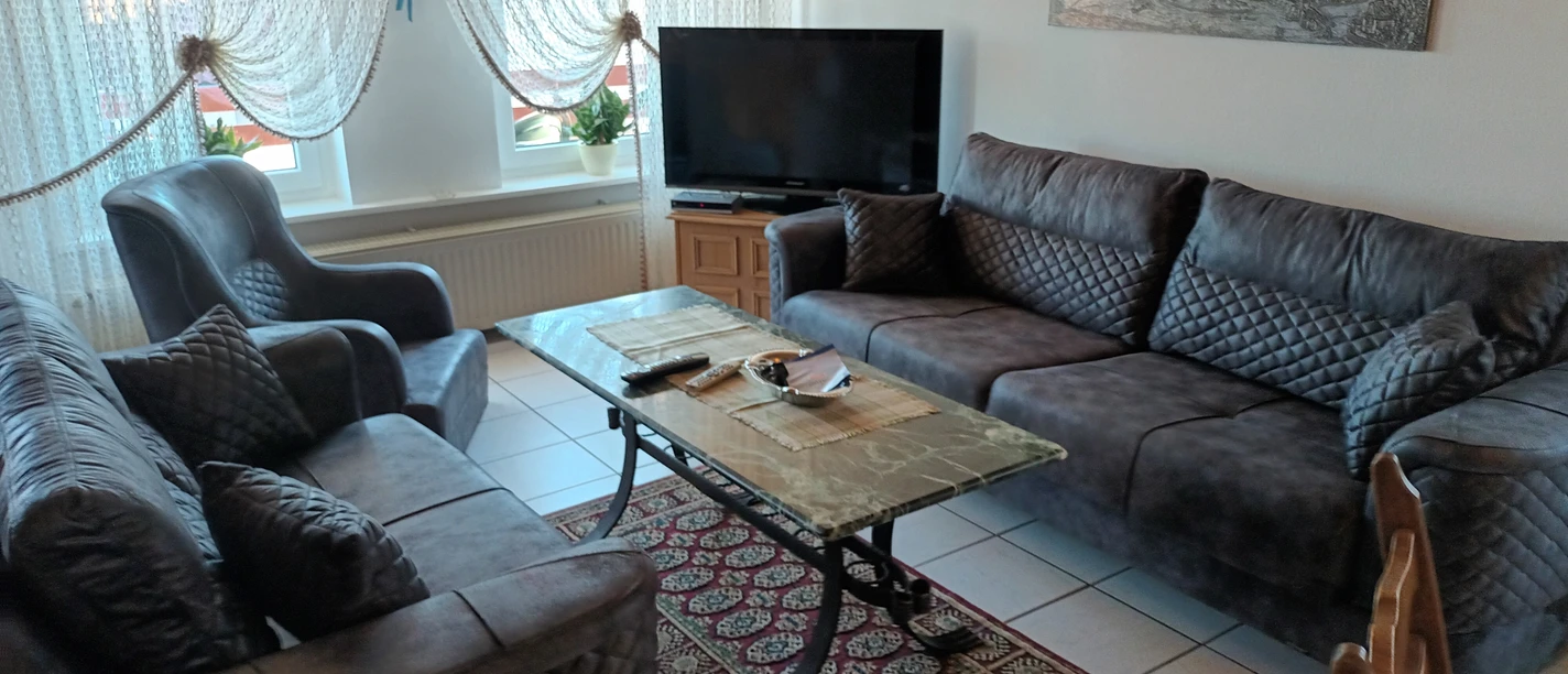 20230908_171435.jpg Ein helles Wohnzimmer mit zwei großen Sofas, einem Sessel, einem Teppich und einem Fernseher.