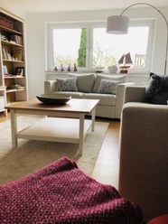 IMG_6222.jpeg Ein helles Wohnzimmer mit zwei Sofas, Couchtisch, Regal, maritimen Dekorationen und großem Fenster.