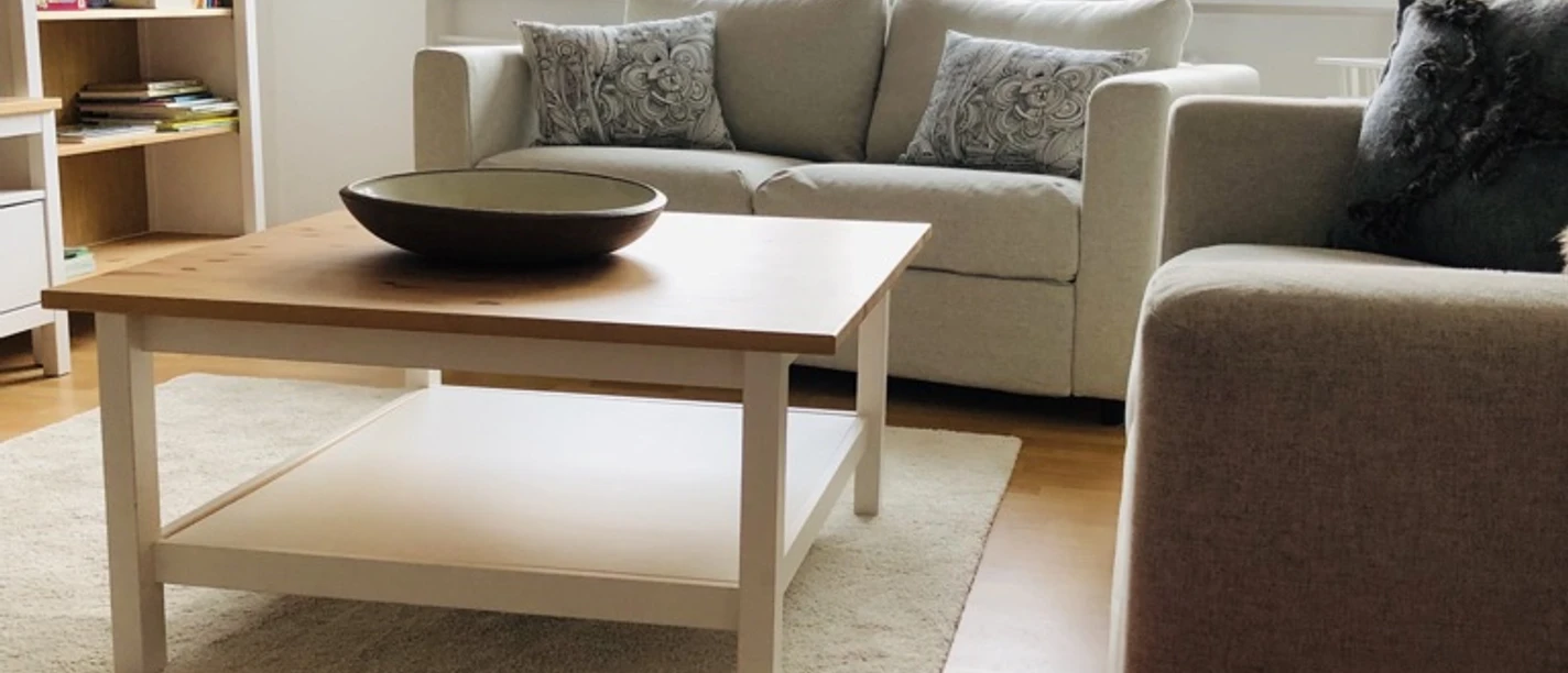 IMG_6222.jpeg Ein helles Wohnzimmer mit zwei Sofas, Couchtisch, Regal, maritimen Dekorationen und großem Fenster.