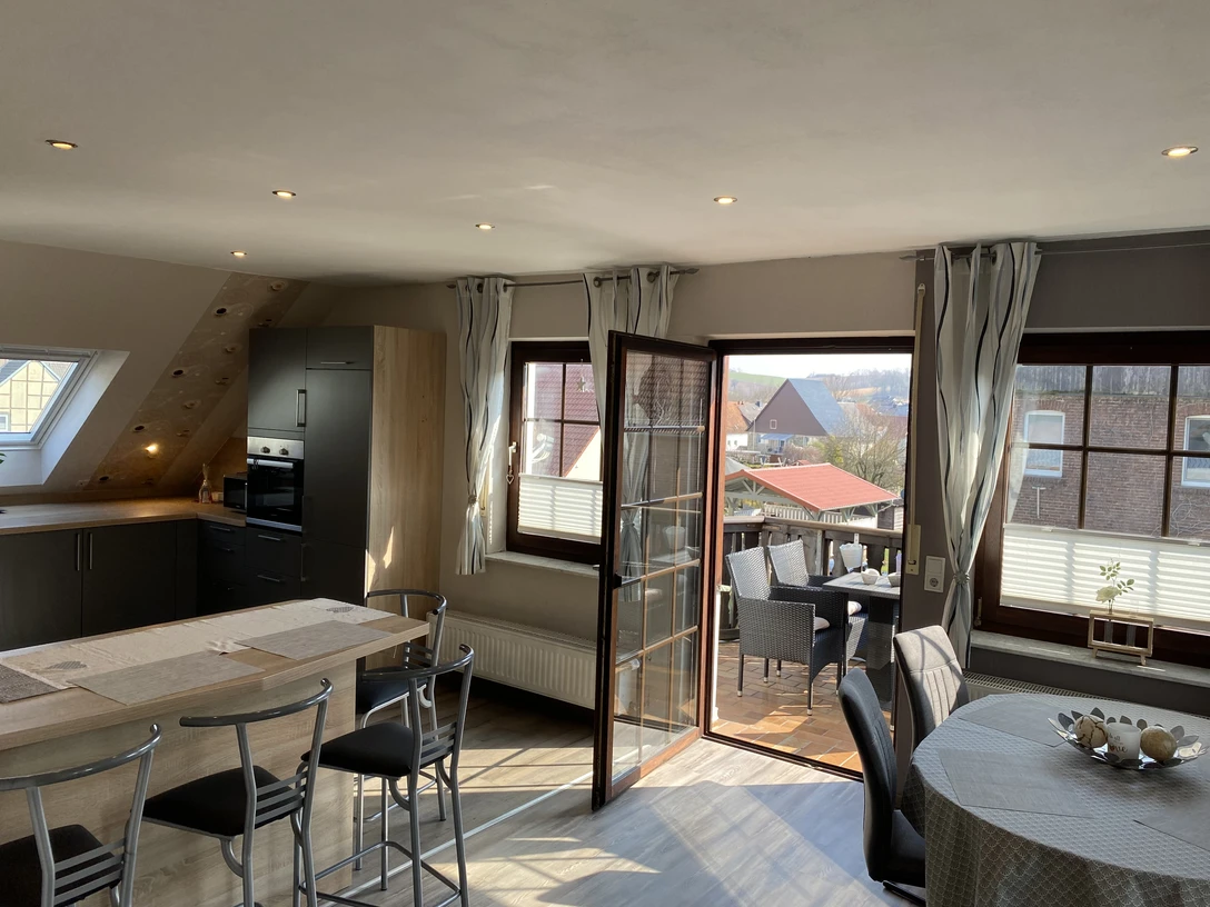 IMG_2115.jpeg Helle, moderne Küchenzeile mit angrenzendem Esstisch, offener Zugang zu einem Balkon mit Sitzmöbeln.