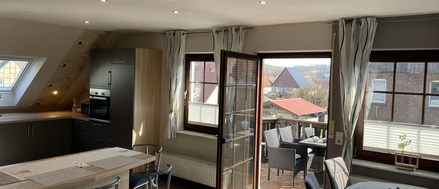 IMG_2115.jpeg Helle, moderne Küchenzeile mit angrenzendem Esstisch, offener Zugang zu einem Balkon mit Sitzmöbeln.