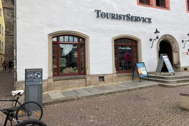 Pirna e-bike charging station Tourist information center with white façade and red windows, next to it an e-bike charging station and a bicycle in the foreground.