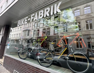 Bike-Fabrik Fahrradgeschäft mit modernen Bikes im Schaufenster und Spiegelung von Altbauarchitektur.