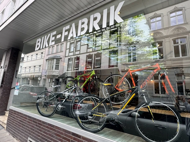 Bike-Fabrik Fahrradgeschäft mit modernen Bikes im Schaufenster und Spiegelung von Altbauarchitektur.