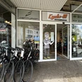 Cycle-M Fahrradgeschäft mit verschiedenen Fahrradmodellen und Zubehör im Schaufenster, Eingang mit Figur.