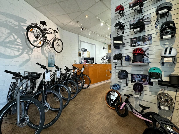 Cycle-M Fahrradgeschäft mit modernen Rädern und Helmen an weißen Wänden, hölzerner Tresen im Hintergrund.