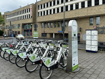 E-Bike Verleihstation Bergisch Gladbach Reihe von Elektrofahrrädern an einer Leihstation vor einem modernen, mehrstöckigen Gebäude.