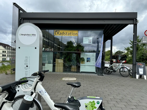 E-Bike Verleihstation Fahrradstation mit E-Bikes und Ladestation vor einem modernen Gebäude mit großen Glasfenstern.