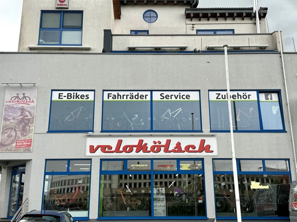 Velokölsch Fahrradgeschäft "velokölsch" mit Schild im Schaufenster für E-Bikes, Fahrräder, Service und Zubehör.