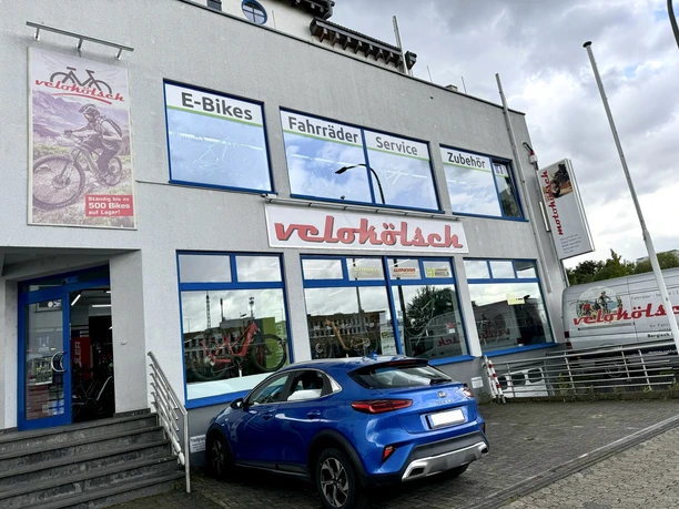 Velokölsch Geschäftsfassade eines Fahrradladens namens "velohölzl" mit Schildern zu E-Bikes, Fahrrädern und Service.