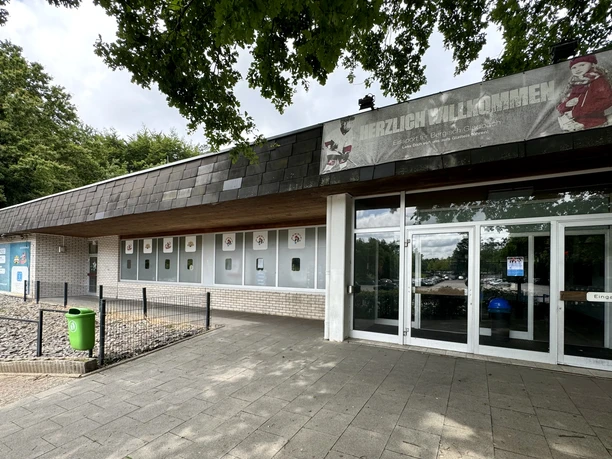 Eissporthalle Eingang eines Gebäudes mit Glasfront, weißer Ziegelfassade und einem Banner am Dachvorsprung.