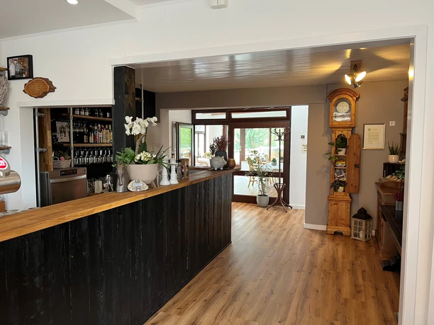 Een gezellig interieur met een houten vloer, een bar en een antieke staande klok op de achtergrond.