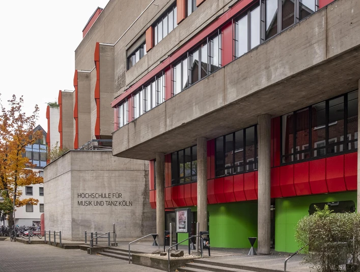 Hochschule für Musik und Tanz Markantes Gebäude der Hochschule für Musik und Tanz Köln mit roten und grünen Akzenten an der Fassade, umgeben von Bäumen und urbaner Architektur.Striking building of the Cologne University of Music and Dance with red and green accents on the façade, surrounded by trees and urban architecture.
