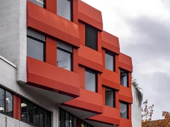 Hochschule für Musik und Tanz Die "Hochschule für Musik und Tanz" zeigt eine moderne Fassade mit markanten roten Fenstern und kantigem Design.The "Hochschule für Musik und Tanz" has a modern façade with striking red windows and an angular design.