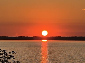 Leuchtender Sonnenuntergang über ruhigem Wasser, reflektiert kräftige Orangetöne am klaren Himmel.