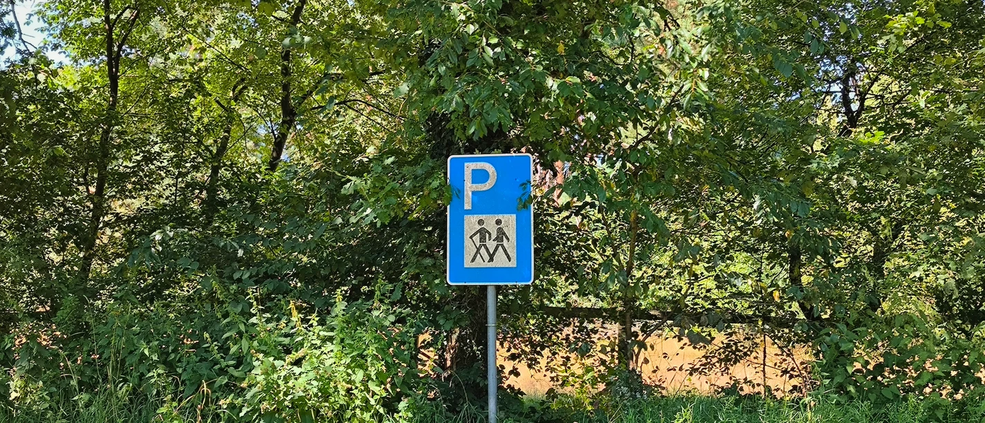 Parkplatzschild für Wanderer umgeben von grünen Bäumen, ein sonniger Tag in einer Waldlichtung.